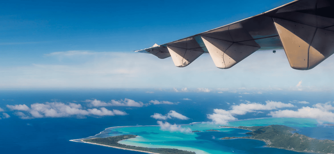 View of an airplane wing over the Caribbean with clear blue water