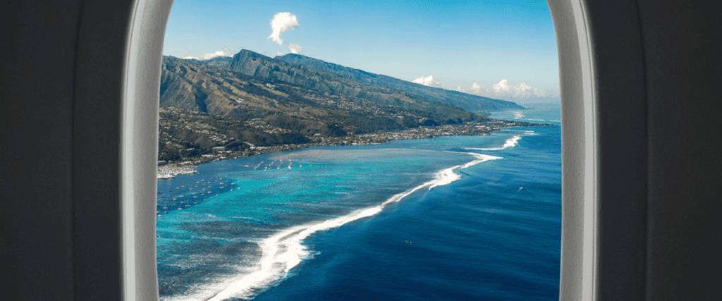 View out an airplane window of a Caribbean island with clear blue water and mountains