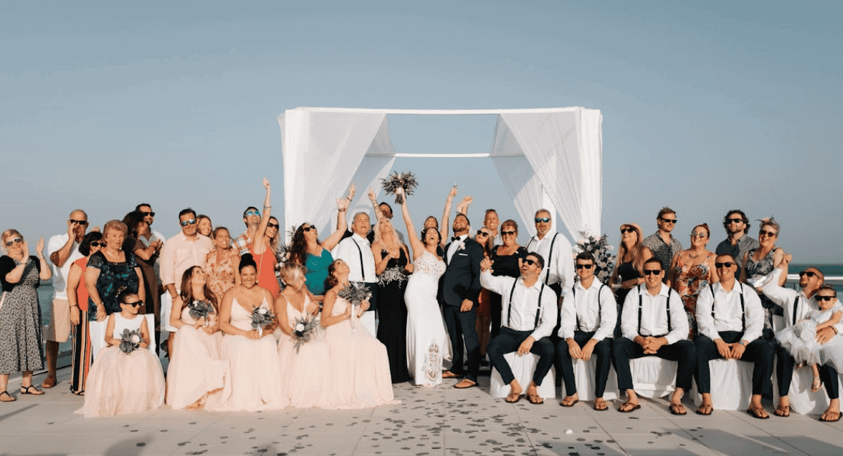 Picture of bride and groom on a beach with the wedding party and all the guest at a destination wedding