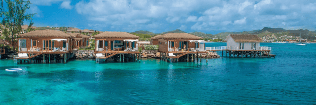 Four over the water bungalows with decks that have ladders going into the ocean with other bungalows in the backgound