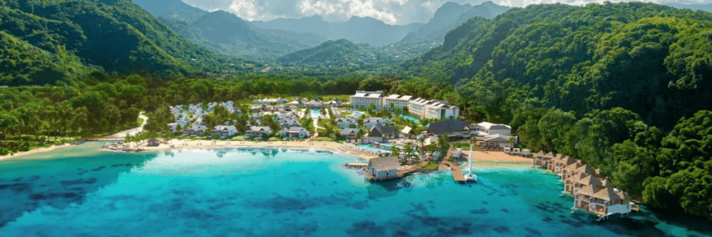 Aerial view of an all inclusive resort on the ocean that is surrounded by green forest mountains