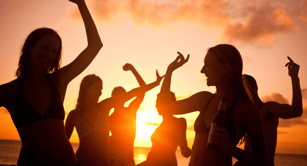 Group of girls in bathing suits shadowed and dancing with the sunset in the background