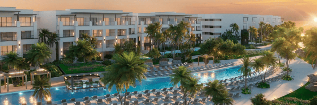 View of buildings at an inclusive resort in Punta Cana with a long pool in front of the buildings with beach chairs surrounding the pool and palm trees throughout the resort