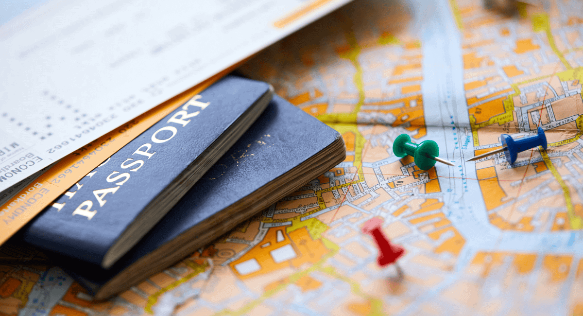 Close up of two plane tickets laying on top of two passports on top of a white and orange map with three colorful pushpins next to it.
