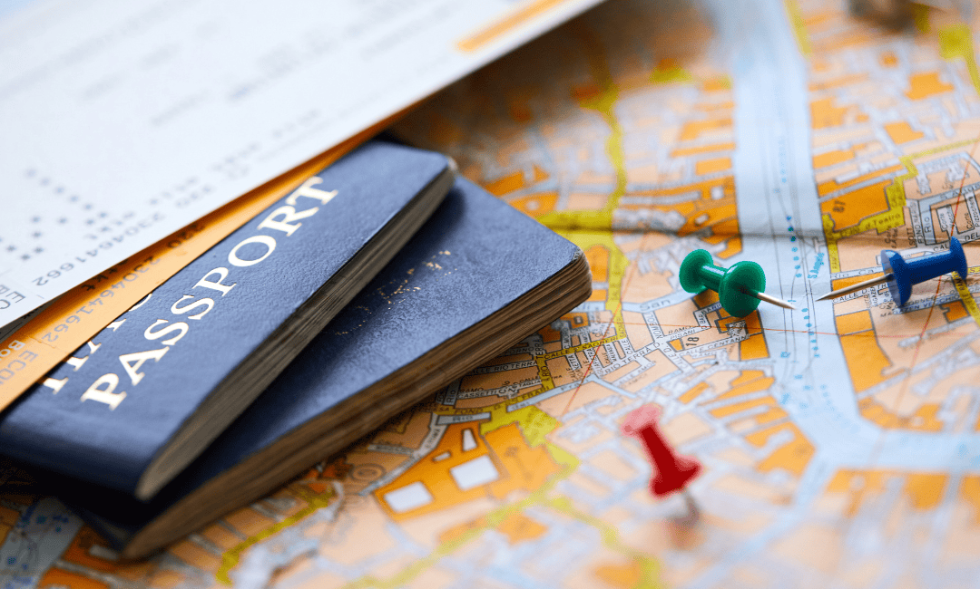 Close up of two plane tickets laying on top of two passports on top of a white and orange map with three colorful pushpins next to it.