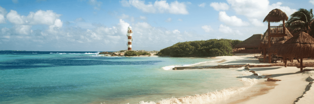 Beach view of beautiful Mexico waters with a red and white lighthouse in the distance and tiki huts on the beach