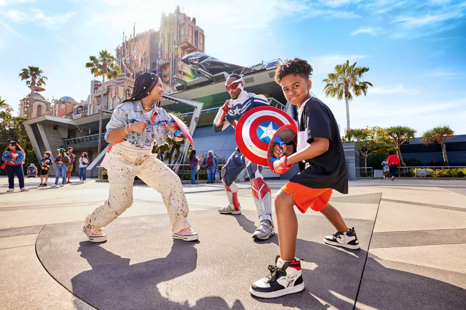 JT-Disney-07 Two children pose with a Captain America performer holding shields at a Disney theme park attraction on a sunny day.