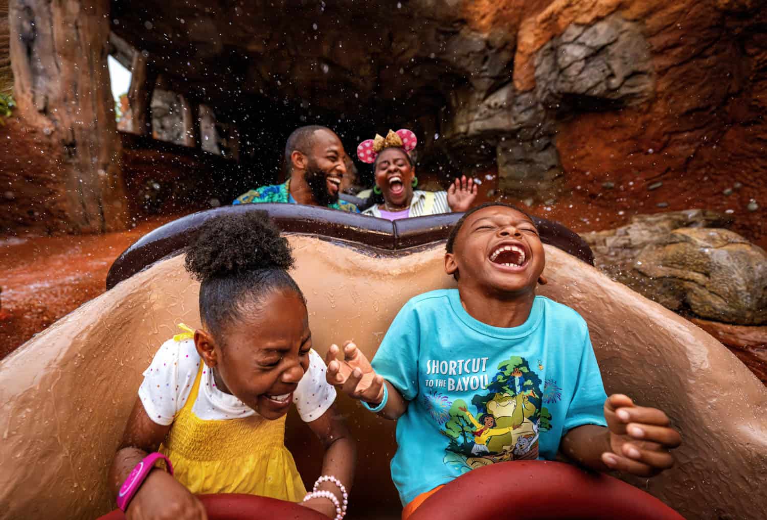 JT-Disney-10 Four people ride a log flume, laughing and reacting to water splashes, with a rocky background on a Disney family vacation.