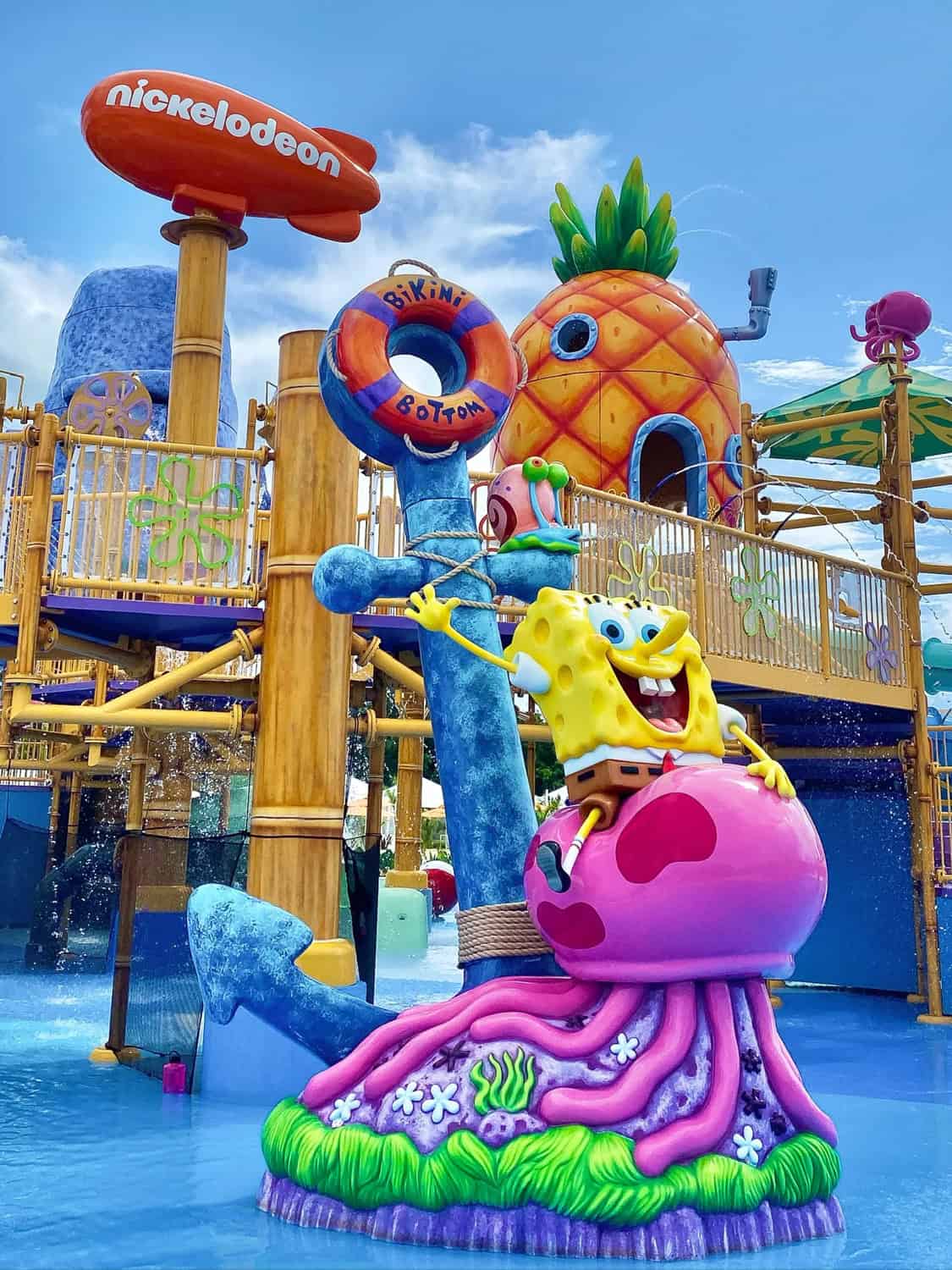 JT-Family-Travel-06 Large SpongeBob SquarePants statue sitting on a pink jellyfish near an anchor, with a pineapple house and Nickelodeon sign in a colorful water play area.