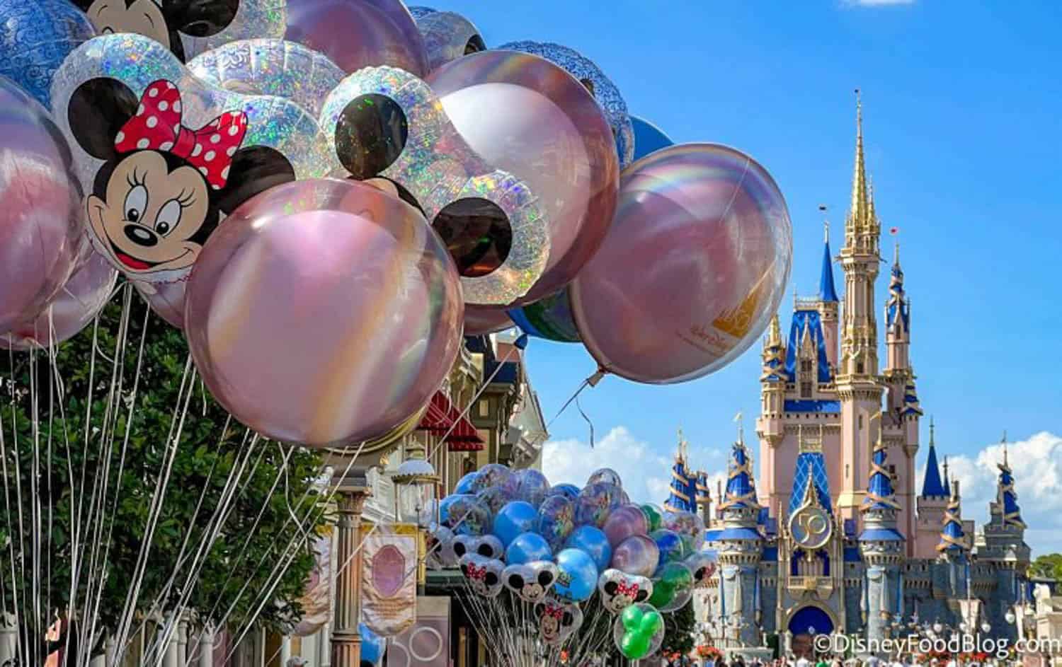 Anna-Swenson-05 Balloons featuring Disney characters float near a street with Cinderella Castle in the background at a Disney theme park.