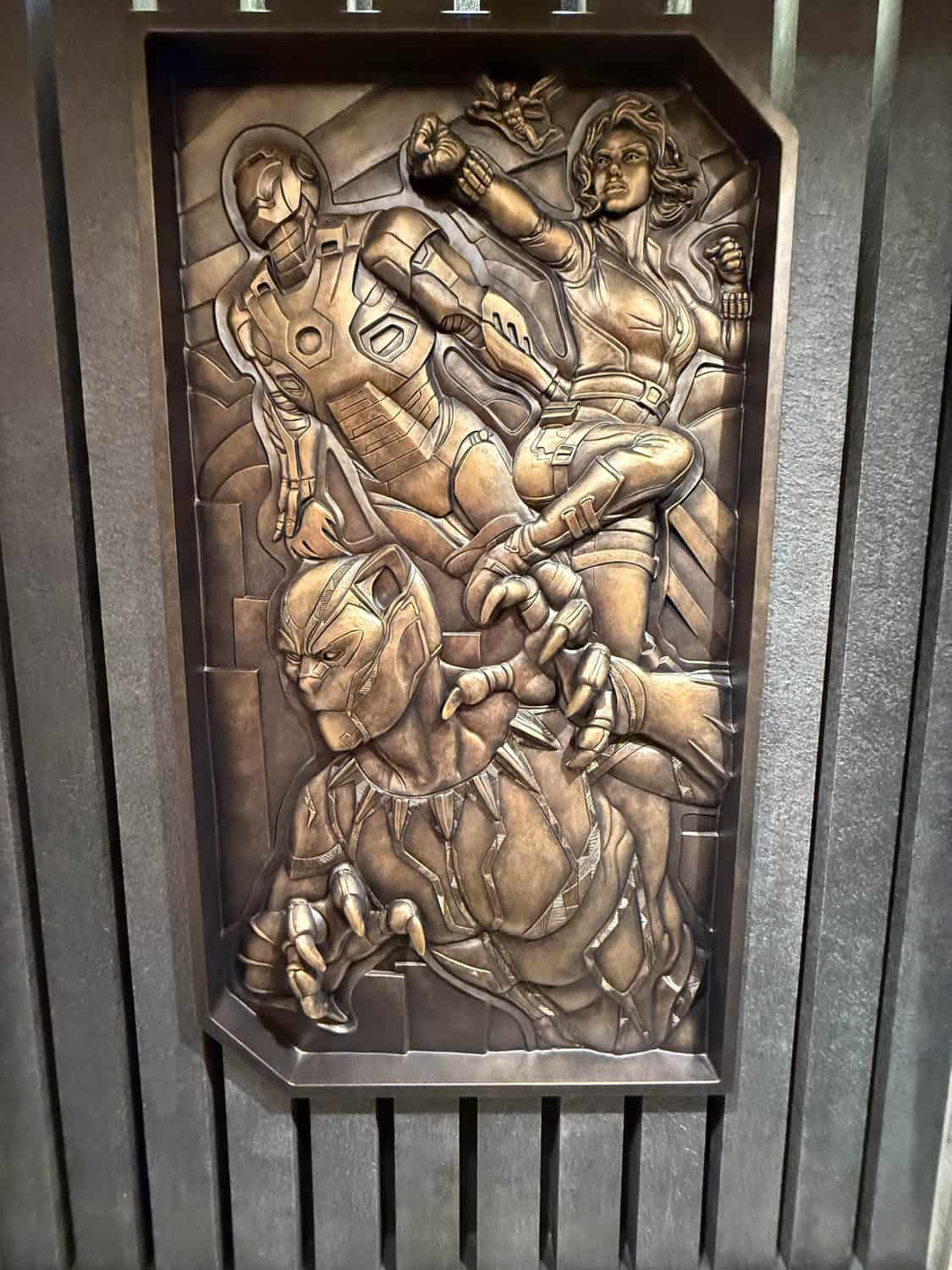 Bronze sculpture depicting three superheroes in dynamic poses, including a figure in a panther suit, a flying armored figure, and a woman with clenched fists.