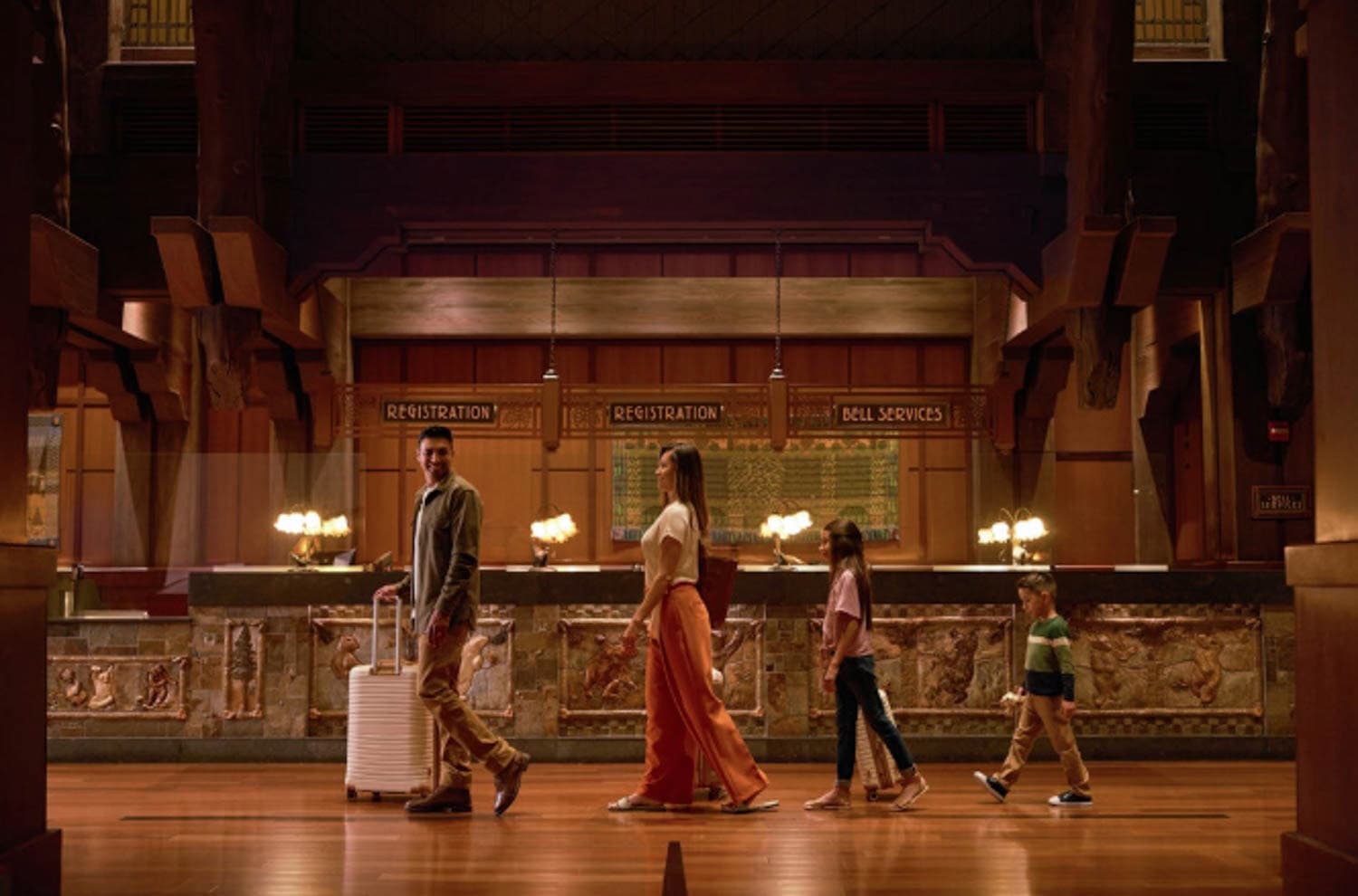 Screenshot A family of four on vacation, walks through a hotel lobby with carved decor and signs for registration and bell services in the background.
