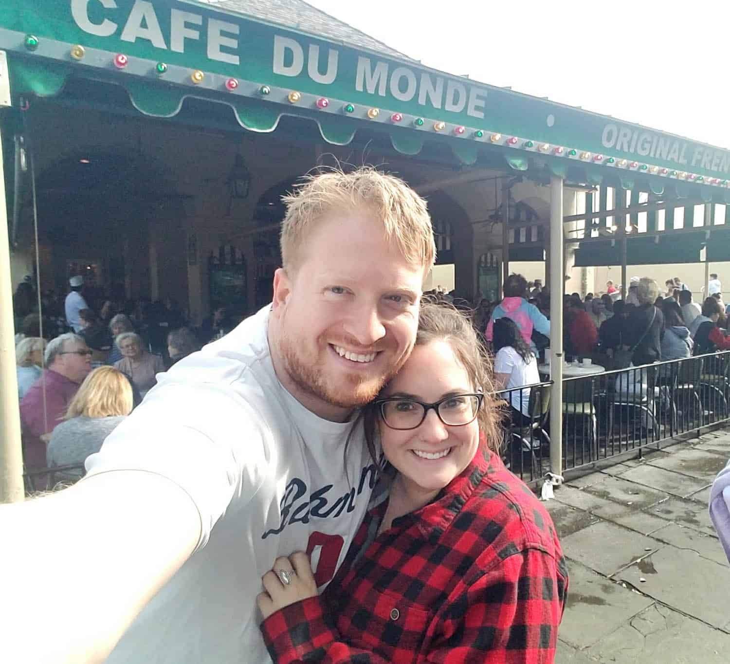 Kristin-Mills-14 A smiling couple takes a selfie in front of the crowded Cafe Du Monde in New Orleans.