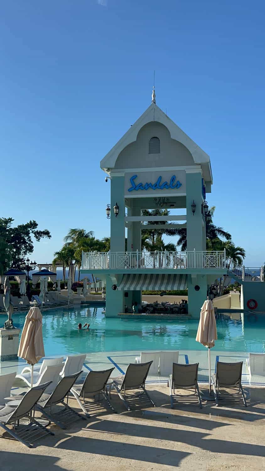 Madelynn-Pierce-06 A poolside view of the Sandals resort tower, with lounge chairs and umbrellas in the foreground and clear blue sky above.