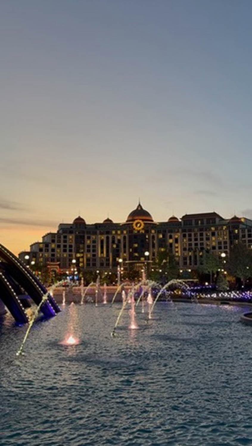 Madelynn-Pierce-10 A large building with domed rooftops is seen behind a lit fountain pool at dusk, with lights illuminating the water and the sky fading from blue to orange.