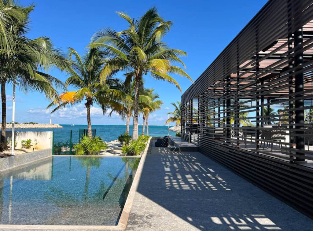 Modern building and poolside area with palm trees overlooking the ocean under a clear blue sky in Mexico.
