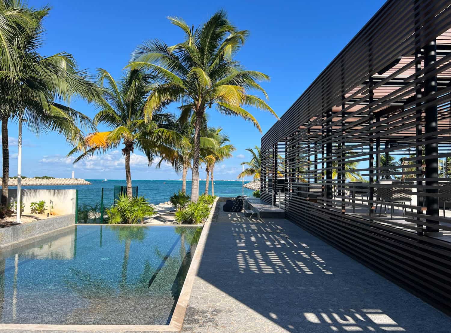 Modern building and poolside area with palm trees overlooking the ocean under a clear blue sky in Mexico.