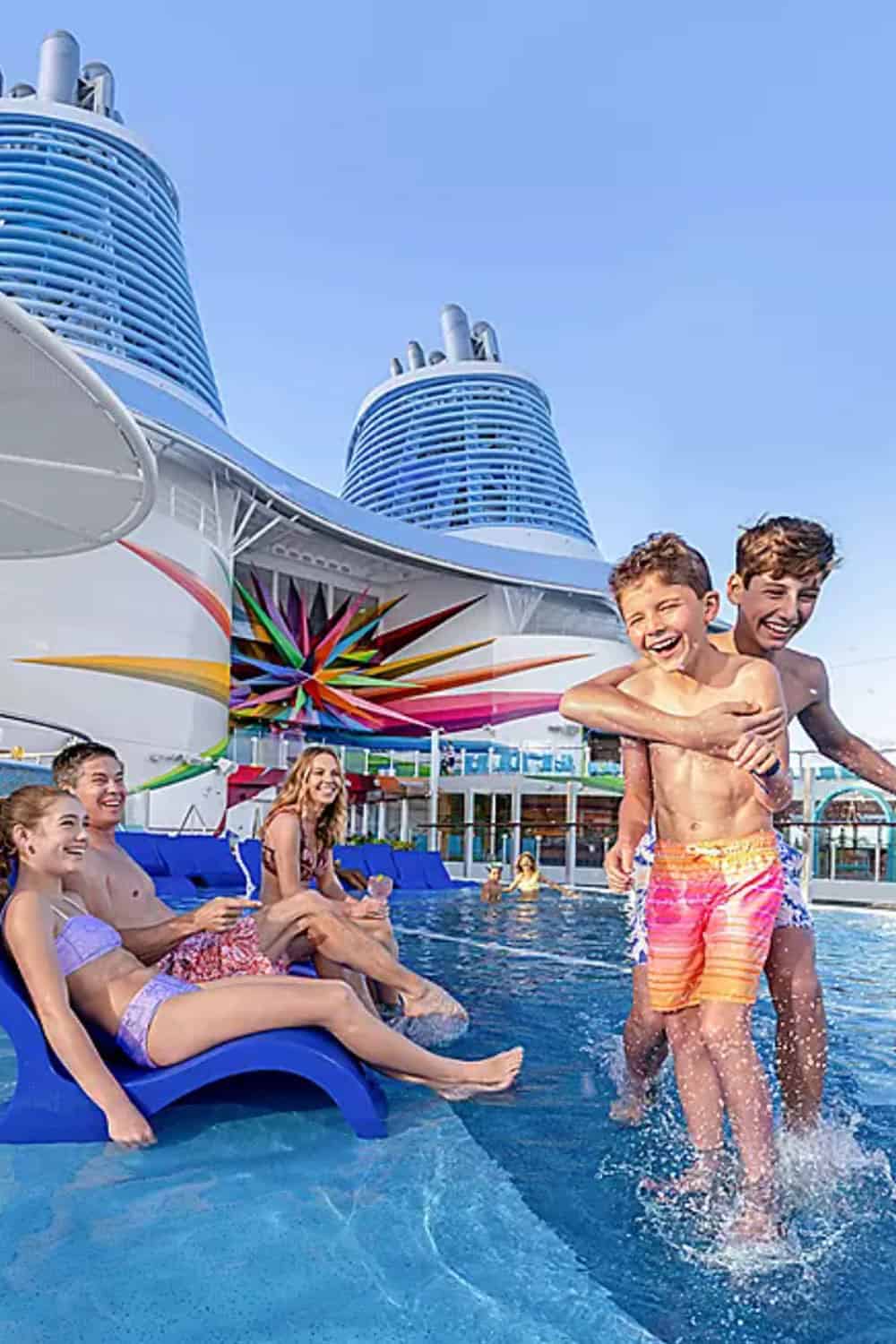 Children and teenagers play and lounge in a pool on a cruise ship, with colorful decor and large funnels visible in the background.